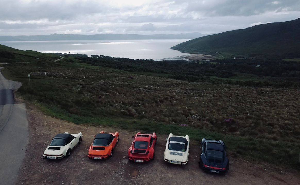 Fünf Porsche 911 in Reihe an der schottischen Küste — NC500-Tour, Drohnenaufnahme