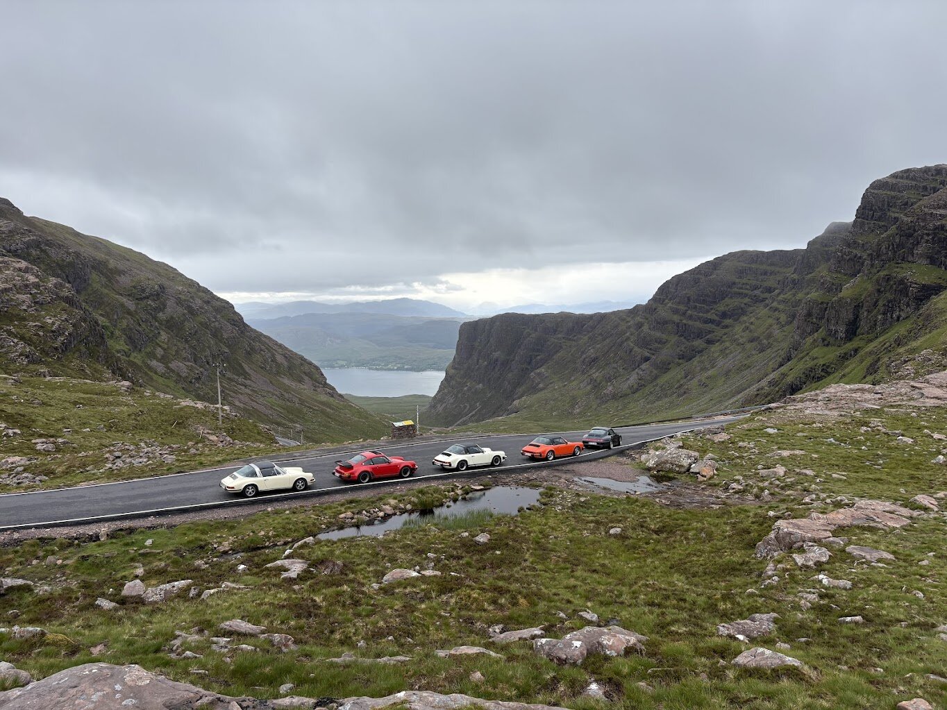 Fünf Porsche in Reihe am Bealach-na-Bá-Aussichtspunkt mit Blick auf den Loch